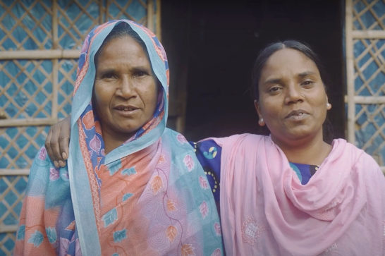 two women in colourful clothes next to each other, the younger one on the right putting her arm around the shoulder of the older lady enxt to her
