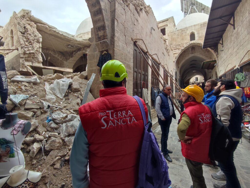 damaged houses rubble men wearing safety helmets