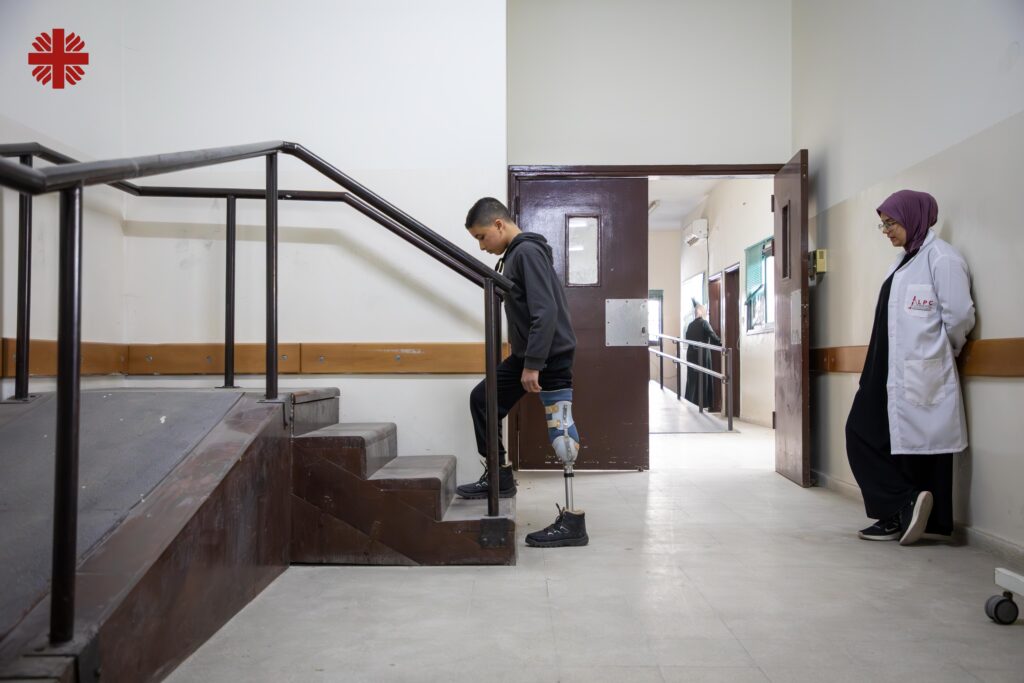 a boy with a prothetic leg goes up a stair case supervised by a medical person