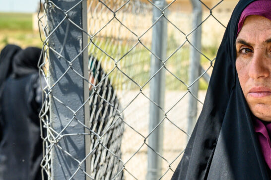 Veiled woman leans against fence in front of health centre