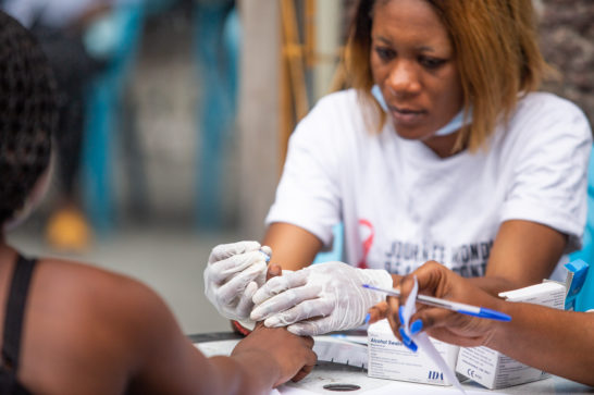 someone in a white shirt carrying medical gloves takes a finger blood test