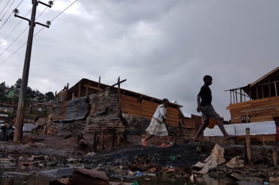 Two figures walk by houses and rubbish