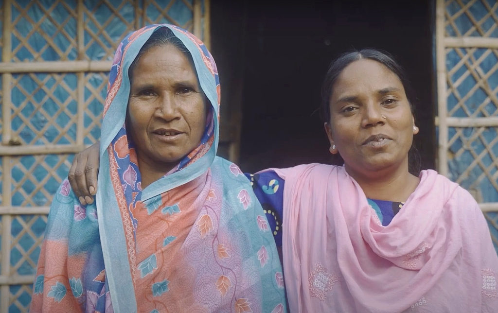 two women in colourful clothes next to each other, the younger one on the right putting her arm around the shoulder of the older lady enxt to her