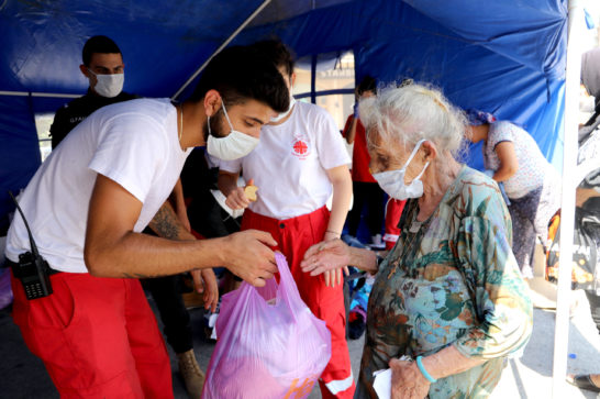 humanitarian relief site aid workers hand out bags to an old lady wearing face masks