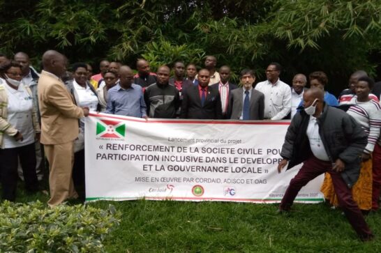 a group of some 30 people in a green garden setting holding a banner