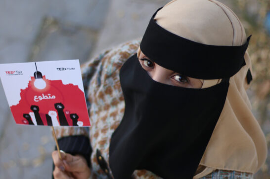 young woman holding a card showing raised fists and looking into the camera