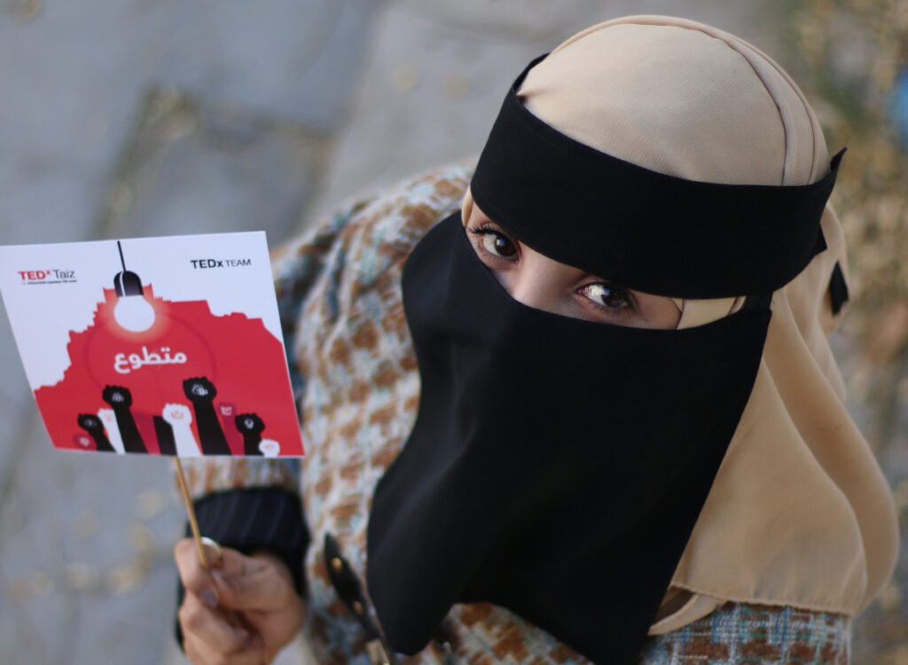 young woman holding a card showing raised fists and looking into the camera