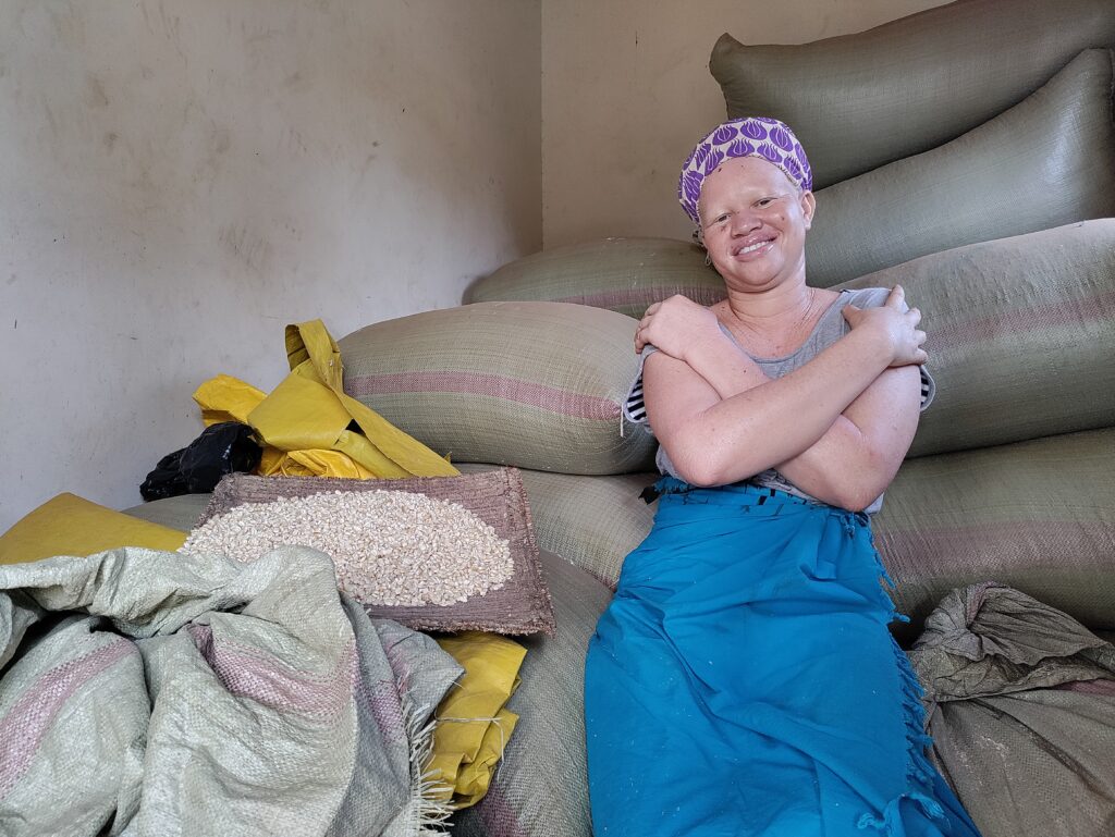 Martha smiles at the camera sat amid bags of her farm produce in her storage facility in Odokomit village.