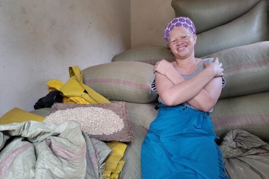 Martha smiles at the camera sat amid bags of her farm produce in her storage facility in Odokomit village.