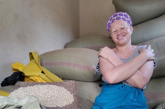 Martha smiles at the camera sat amid bags of her farm produce in her storage facility in Odokomit village.