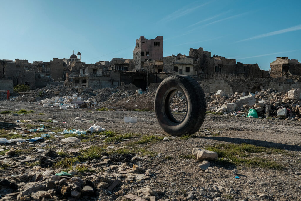 A view of Mosul under a blue sky in the background with a tire and rubble in the foreground.