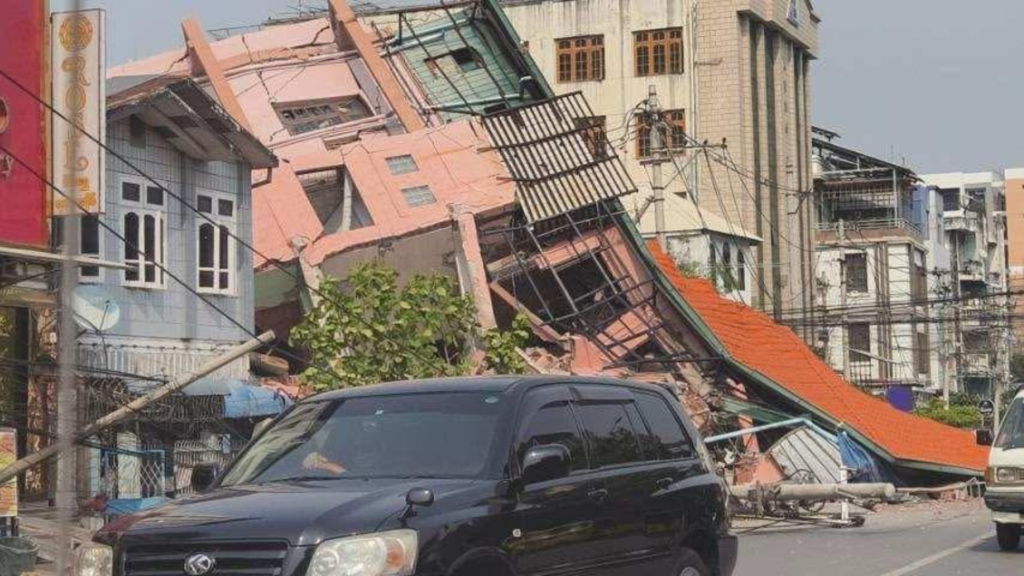 Ingestort woongebouw ligt schuin over een straat in Myanmar na een zware aardbeving; brokstukken, elektriciteitskabels en auto's op de voorgrond tonen de chaos en schade.
