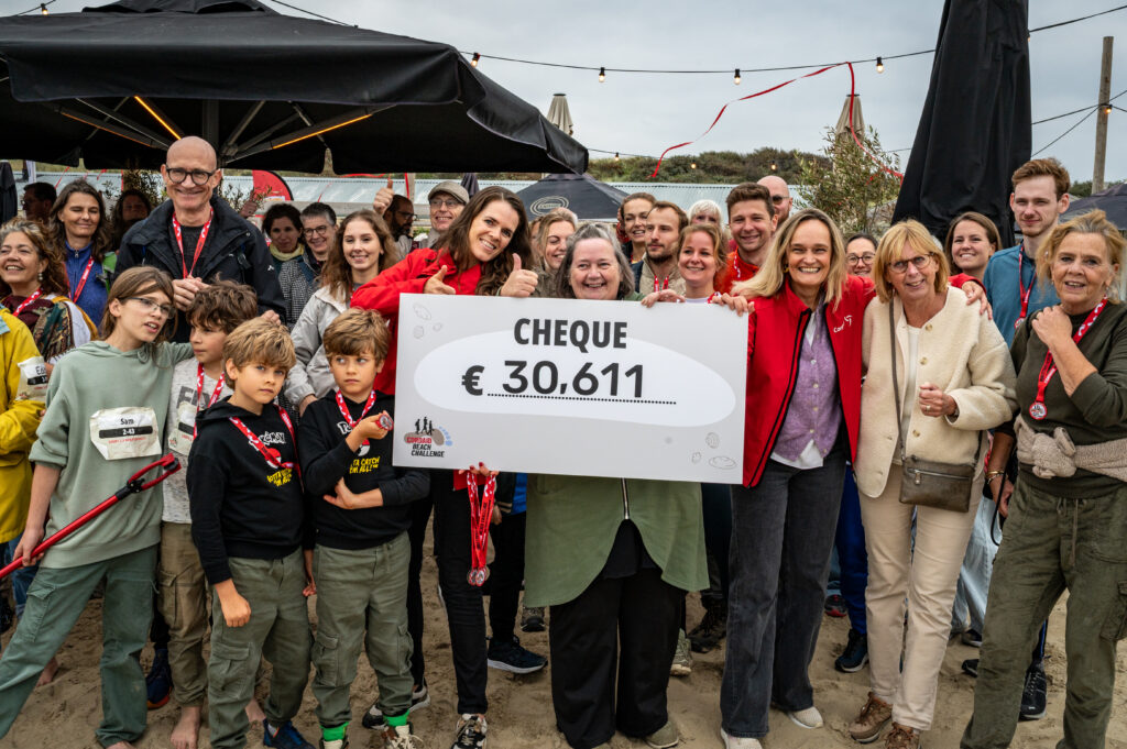 Blije deelnemers en mensen van Cordaid hebben cheque met opgehaald eindbedrag in hun handen op het strand - Cordaid Beach Challenge 2025