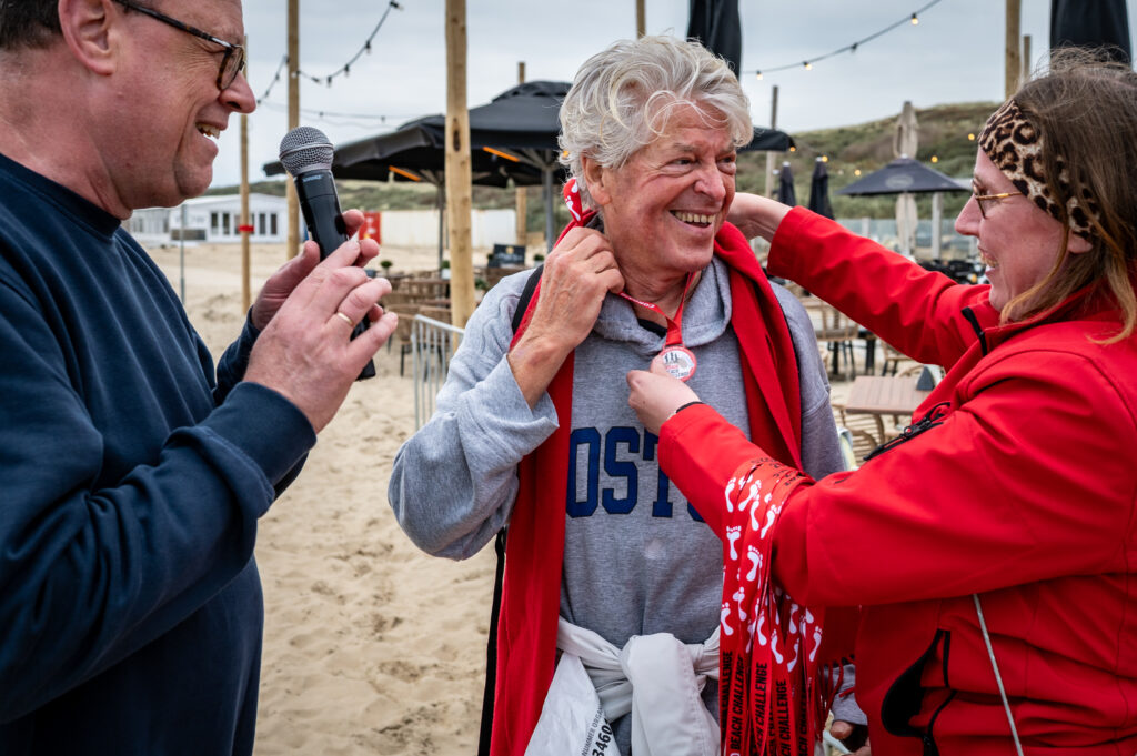 Deelnemer Cordaid Beach Challenge 2025 krijgt medaille van Cordaid medewerker op strand in Scheveningen