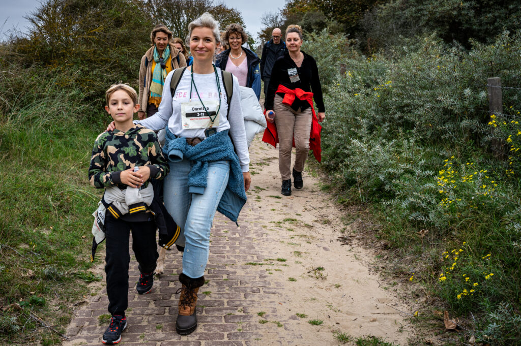 Moeder en zoon lopen met andere deelnemers Cordaid Beach Challenge 2025 in duinen van Scheveningen