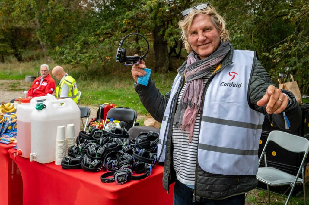 Vrijwilliger deelt koptelefoons uit bij rustpunt van Cordaid Beach Challenge 2025 in Meijendel