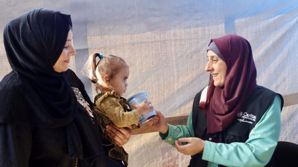 Medewerker Caritas geeft moeder en kind een blik babyvoeding in Gaza - Cordaid