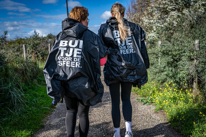 Wandelaars met regenjassen in duinen.